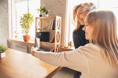 Young friends, women using gadgets to watch cinema, photos, online courses, taking selfie or vlog. Two caucasian female models at home having fun and using laptop, tablet, smartphone, headphones.の写真素材
