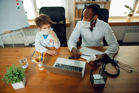 Caucasian teenboy as a doctor consulting, giving recommendation, treating. Little doctor during discussing, studying with older colleague. Concept of childhood, human emotions, health, medicine.の写真素材