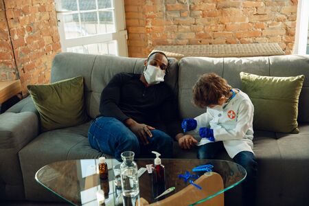 Caucasian teenboy as a doctor consulting for patient at home, giving recommendation, treating. Little doctor during checking up the sick man. Concept of childhood, human emotions, health, medicine.の写真素材