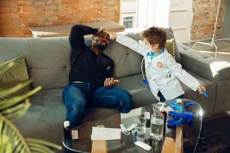 Caucasian teenboy as a doctor consulting for patient at home, giving recommendation, treating. Little doctor taking temperature of sick man. Concept of childhood, human emotions, health, medicine.の写真素材