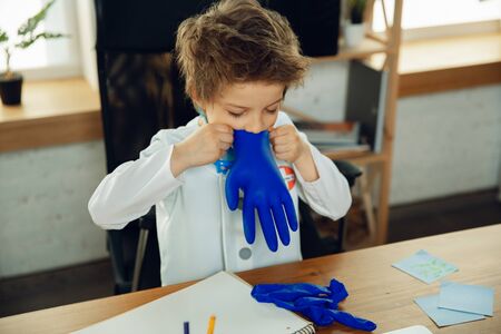 Caucasian teenboy as a doctor consulting for patient, giving recommendation, treating. Little doctor during funny wearing protective gloves. Concept of childhood, human emotions, health, medicine.の写真素材