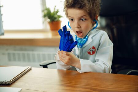 Caucasian teenboy as a doctor consulting for patient, giving recommendation, treating. Little doctor during funny wearing protective gloves. Concept of childhood, human emotions, health, medicine.の写真素材