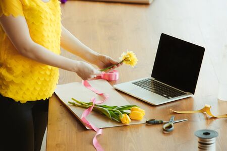 Florist at work: woman shows how to make bouquet with tulips. Young caucasian woman gives online...