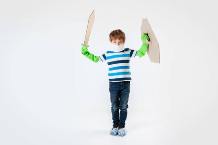 Little caucasian boy as a warrior in fight with coronavirus pandemic, with a shield, a sword and a toilet paper bandoleer. Teenboy in war for human lives. Concept of childhood, health, winning.の写真素材