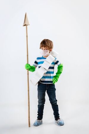 Little caucasian boy as a warrior in fight with coronavirus pandemic, with a face mask, a spear and a toilet paper bandoleer. Teenboy in war for human lives. Concept of childhood, health, winning.の写真素材