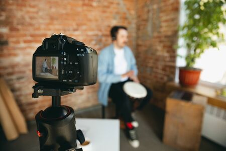 Caucasian musician playing hand drum during online concert at home isolated and quarantined. Using camera, laptop, streaming, recording courses. Concept of art, support, music, hobby, education.の写真素材