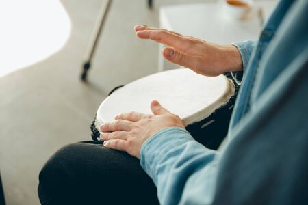 Caucasian musician playing hand drum during online concert at home isolated and quarantined. Using camera, laptop, streaming, recording courses. Concept of art, support, music, hobby, education.の写真素材