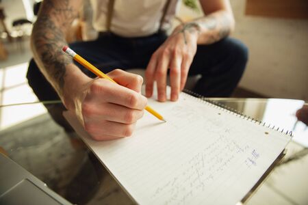 Close up of male hands writing on an empty paper on the table at home. Making notes, workhome,...