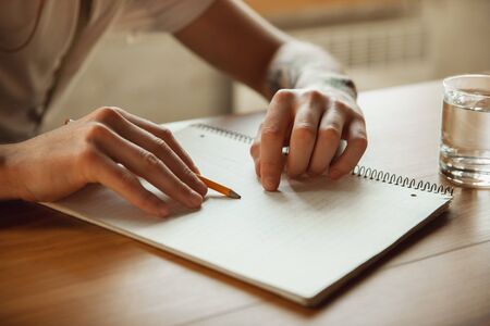 Close up of male hands writing on an empty paper on the table at home. Making notes, workhome,...