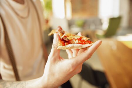 Close up of stylish caucasian man holding pizza, eating, proposing. Focus on hands and ingredients. Concept of food, nutrition, taste. Copyspace for proposal, advertising.の写真素材