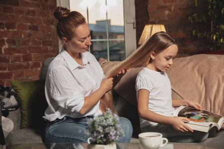 Hairdo, hairstyle. Mother and daughter during self-insulation at home while quarantined, family time cozy and comfort, domestic life. Cheerful and happy smiling models. Safety, prevention, love concept.の写真素材