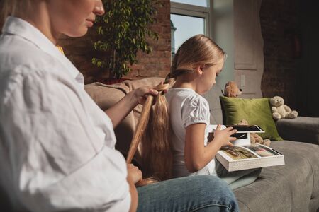 Hairdo, hairstyle. Mother and daughter during self-insulation at home while quarantined, family time cozy and comfort, domestic life. Cheerful and happy smiling models. Safety, prevention, love concept.の写真素材