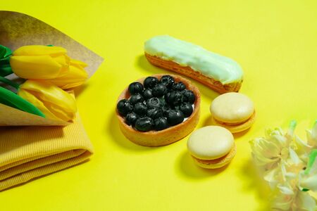Macaroons and flowers. Monochrome stylish and trendy composition in yellow color on studio background. Top view, flat lay. Pure beauty of usual things around. Copyspace for ad. Holiday, food, fashion.の写真素材