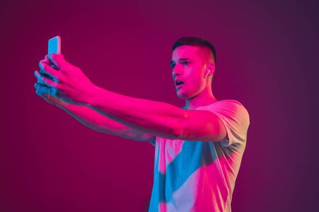 Surfing, betting, watching, selfie. Caucasian mans portrait isolated on pink-purple studio...