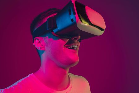 Playing with VR, shoting, driving. Caucasian mans portrait isolated on pink-purple studio background...
