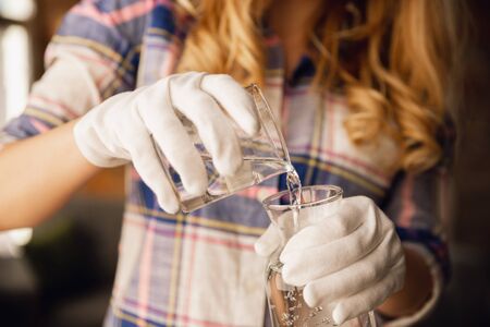 Close up of female hands in gloves holding bottle and glass, pouring pure water. Healthy lifestyle, health care, diet. Preparing, proposing for somebody. Copyspace. Water purification, safety.の写真素材