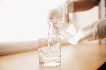 Close up of female hands in gloves holding bottle and glass, pouring pure water. Healthy lifestyle, health care, diet. Preparing, proposing for somebody. Copyspace. Water purification, safety.の写真素材