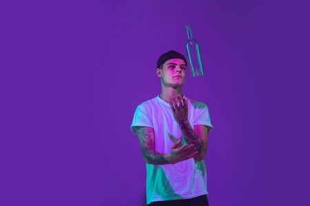 Throws up a bottle of water. Caucasian mans portrait isolated on purple studio background in pink...