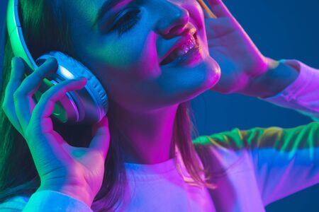Listening to music. Caucasian young womans portrait isolated on blue studio background in neon light. Beautiful female model. Concept of human emotions, facial expression, sales, ad, youth culture.の写真素材