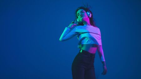 Listening to music. Caucasian young womans portrait isolated on blue studio background in neon light. Beautiful female model. Concept of human emotions, facial expression, sales, ad, youth culture.の写真素材
