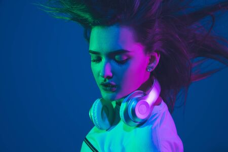 Flying hair. Caucasian young womans portrait isolated on blue studio background in neon light. Beautiful female model. Concept of human emotions, facial expression, sales, ad, youth culture.の写真素材