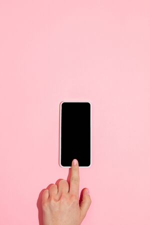 Hand using gadget, smartphone on top view, blank screen with copyspace, minimalistic style. Technologies, modern, marketing. Negative space for advertising. Coral color on background. Stylish, trendy.の写真素材