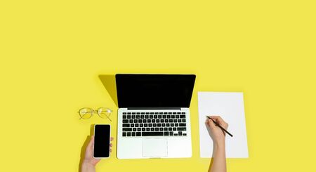 Hand using gadgets, devices on top view, blank screen with copyspace, minimalistic style. Technologies, modern, marketing. Negative space for ad, flyer. Yellow color on background. Stylish, trendy.の写真素材