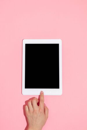 Hand using gadgets, tablet on top view, blank screen with copyspace, minimalistic style. Technologies, modern, marketing. Negative space for advertising. Coral color on background. Stylish, trendy.の写真素材