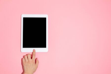 Hand using tablet, device on top view, blank screen with copyspace, minimalistic style. Technologies, modern, marketing. Negative space for advertising. Coral color on background. Stylish, trendy.の写真素材