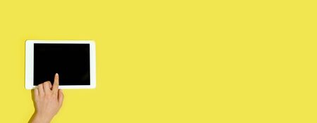 Hand using gadgets, tablet on top view, blank screen with copyspace, minimalistic style. Technologies, modern, marketing. Negative space for ad, flyer. Yellow color on background. Stylish, trendy.の写真素材