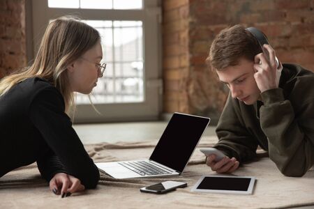 Attractive young couple using devices together, tablet, laptop, smartphone, headphones wireless. Communication, gadgets concept. Technologies connecting people in self-insulation. Lifestyle at home.の写真素材