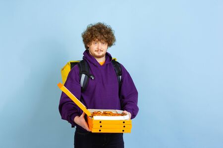Confident opening pizza boxes. Emotions of caucasian deliveryman isolated on blue background....