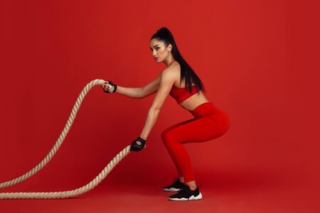 Training active. Beautiful young female athlete practicing in studio, monochrome red portrait. Sportive fit brunette model with ropes. Body building, healthy lifestyle, beauty and action concept.の写真素材