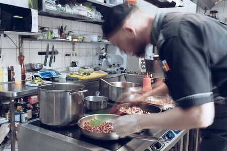 Behind the scenes of brands. The chef cooking in a professional kitchen of a restaurant meal for client or delivery. Open business from the inside. Meals during the quarantine. Hurrying up, motion.の写真素材