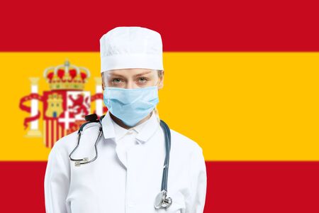 Female young doctor with stethoscope and face mask praying for God with Spain national flag on background. Concept of healthcare and medicine, coronavirus pandemic, danger epidemic, COVID.の写真素材