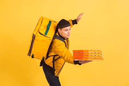 Trying to catch pizzas. Emotions of caucasian deliveryman isolated on yellow background. Contacless delivery service during quarantine. Man delivers food during isolation. Safety. Hurrying up.の写真素材