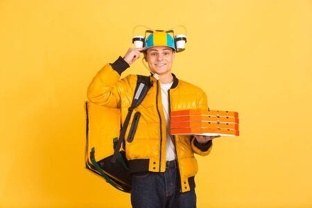 Holding pizza, pointing at head. Emotions of caucasian deliveryman isolated on yellow background....