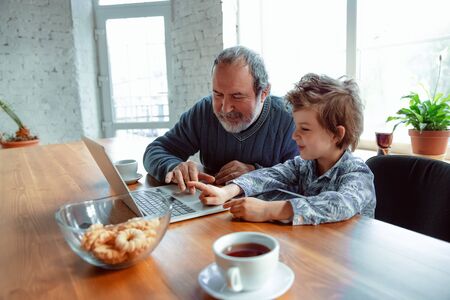 Using devices. Grandfather and his grandson spending time together insulated at home. Having fun, stadying online, reading and cleaning up. Concept of quarantine, family, love, realtions, togetherness.の写真素材