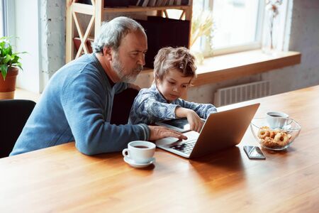 Using devices. Grandfather and his grandson spending time together insulated at home. Having fun,...