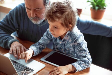 Using devices. Grandfather and his grandson spending time together insulated at home. Having fun,...