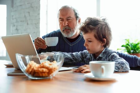 Using devices. Grandfather and his grandson spending time together insulated at home. Having fun,...