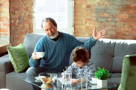 Useful time. Grandfather and his grandson spending time together insulated at home. Having fun,...