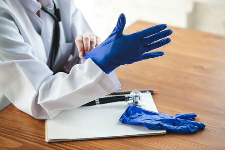 Close up of doctors hands wearing blue protective gloves on wooden table background. Preparing for working. Doctor during his work with patients, explaining recipes for drug, consulting, treating.の写真素材