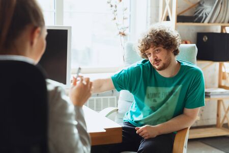 Young man sitting in office during the job interview with female employee, boss or HR-manager,...