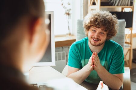 Young man sitting in office during the job interview with female employee, boss or HR-manager, talking, thinking, looks confident. Concept of work, getting job, business, finance, communication.の写真素材