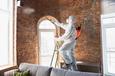 Coronavirus Pandemic. A disinfector in a protective suit and mask sprays disinfectants in house or...