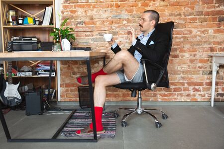 Young man without pants but in jacket working on a laptop.の写真素材