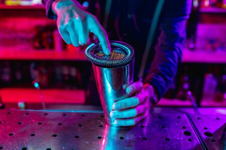 Close up of professional barman finishes preparation of alcoholic cocktail in multicolored neon lightの写真素材