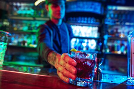 Close up of professional barman finishes preparation of alcoholic cocktail in multicolored neon...