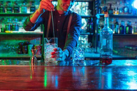Professional barman finishes preparation of alcoholic cocktail for guest in multicolored neon light.の写真素材